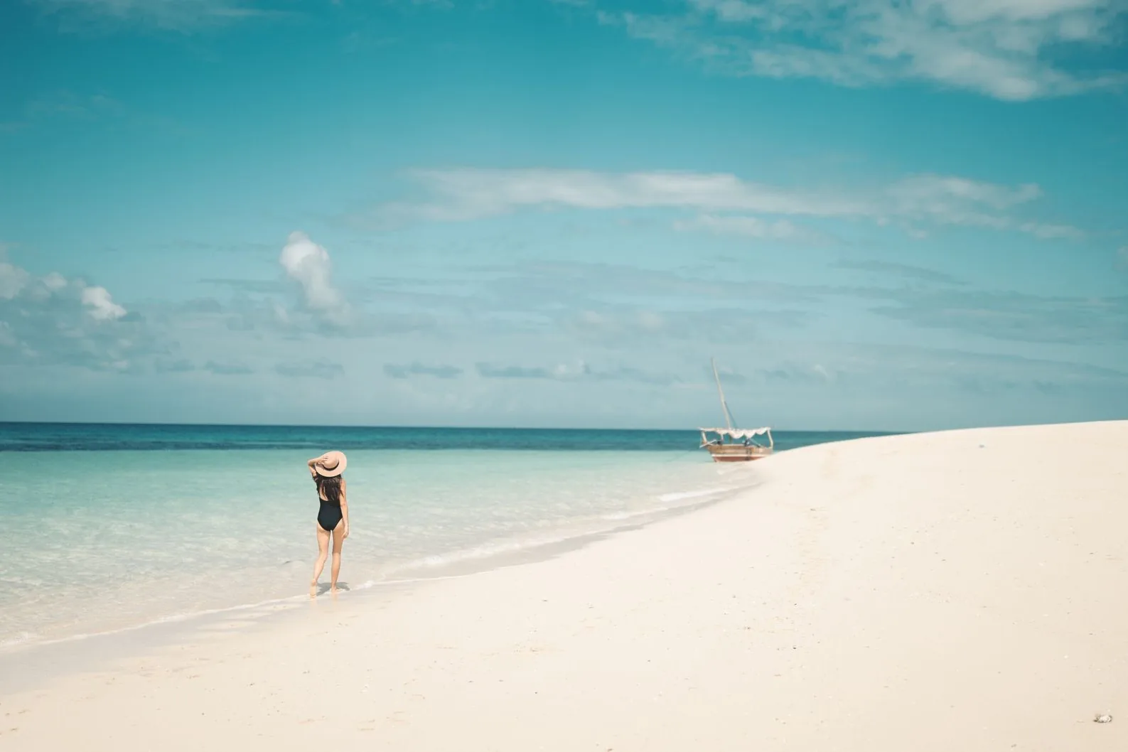 Banc de sable blanc et eau turquoise avec un boutre au large, côte de Zanzibar