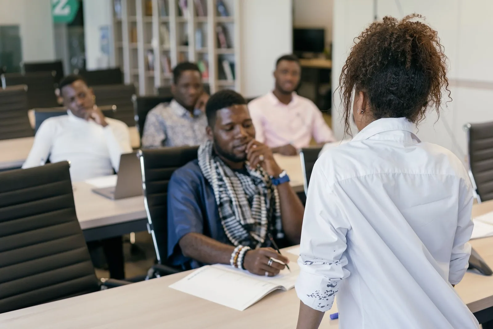 Adultes en cours de langue avec une enseignante debout devant la classe, cahier ouvert et stylo à la main