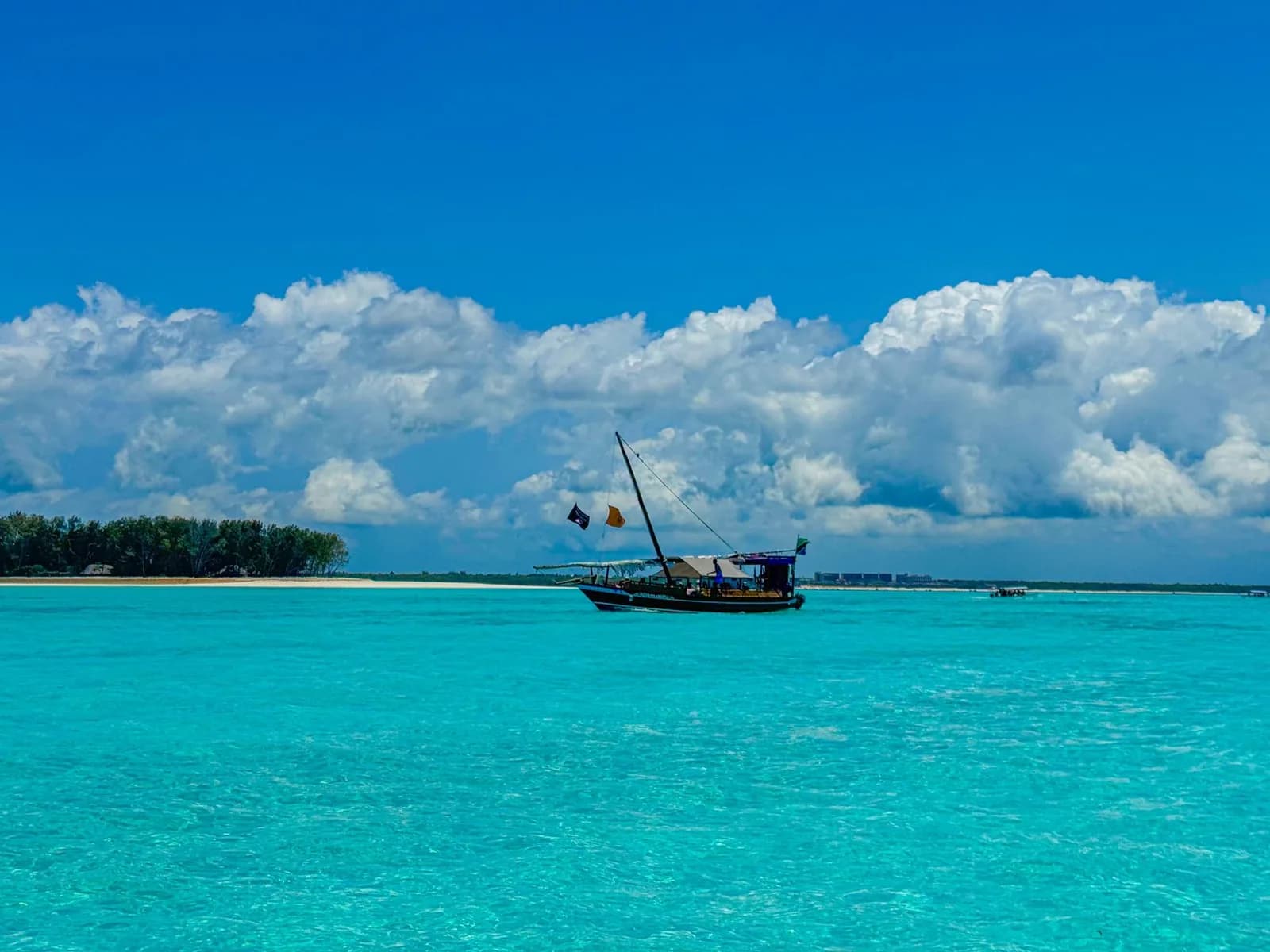 Dhow traditionnel sur un lagon turquoise parfaitement calme, devant un banc de sable et de gros cumulus, à Zanzibar en octobre