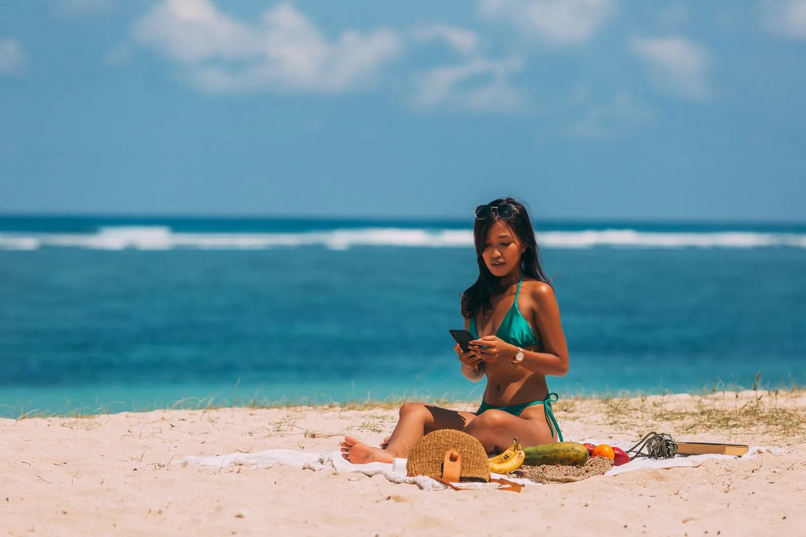 Voyageuse consultant son smartphone sur une plage de sable blanc au bord d'un océan turquoise à Zanzibar