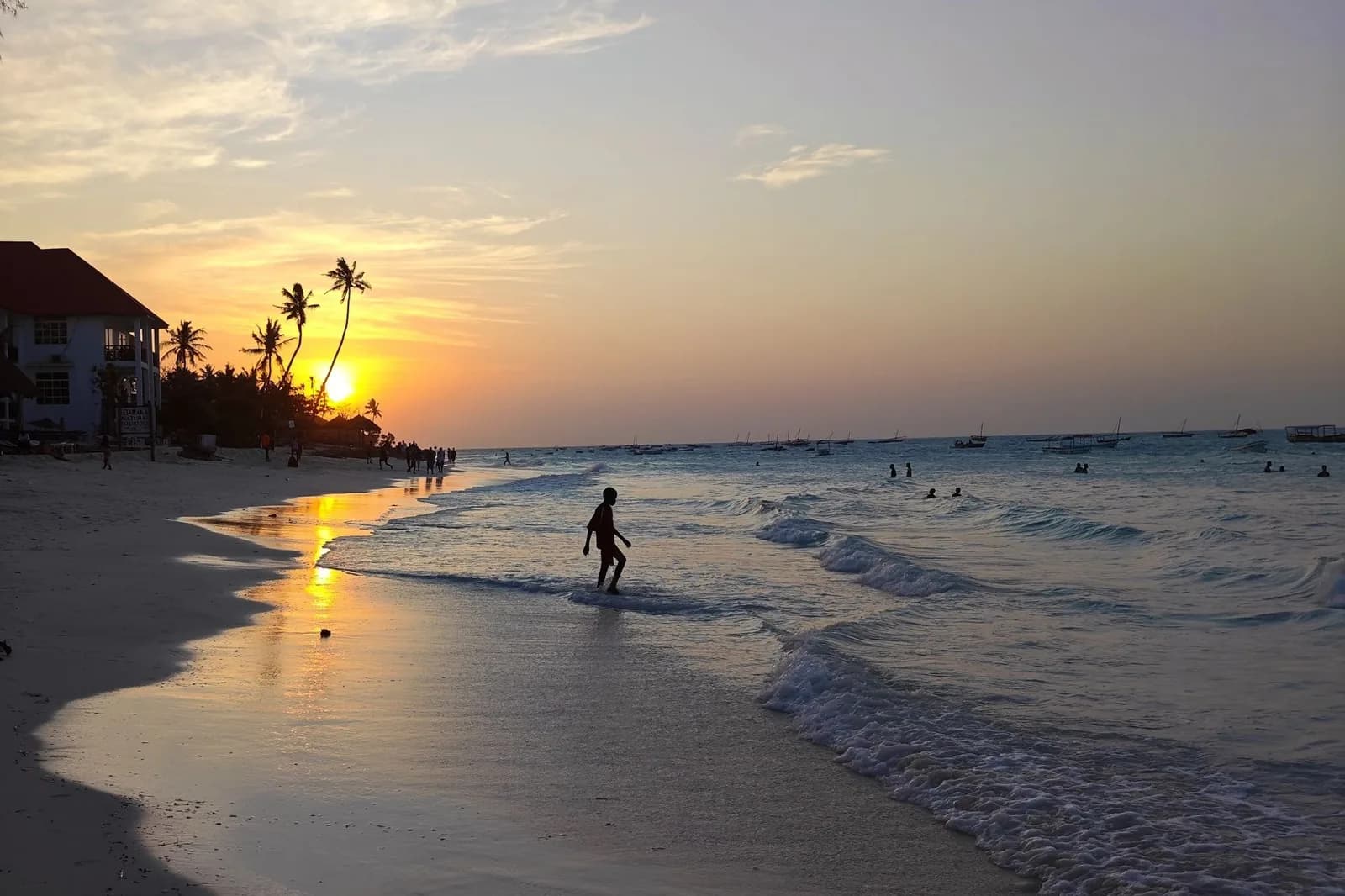 Coucher de soleil sur une plage de sable blanc de la côte nord-ouest de Zanzibar, cocotiers et boutres au large