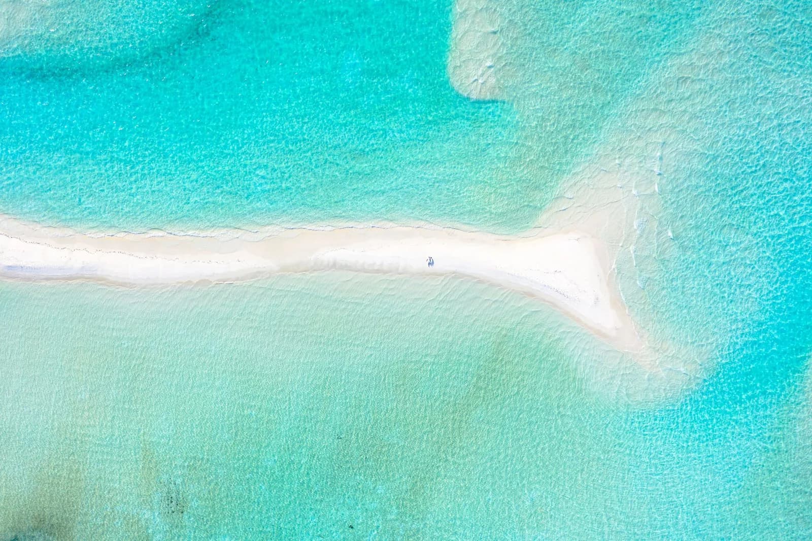 Étroite bande de sable blanc encerclée par la mer qui monte, vue du ciel