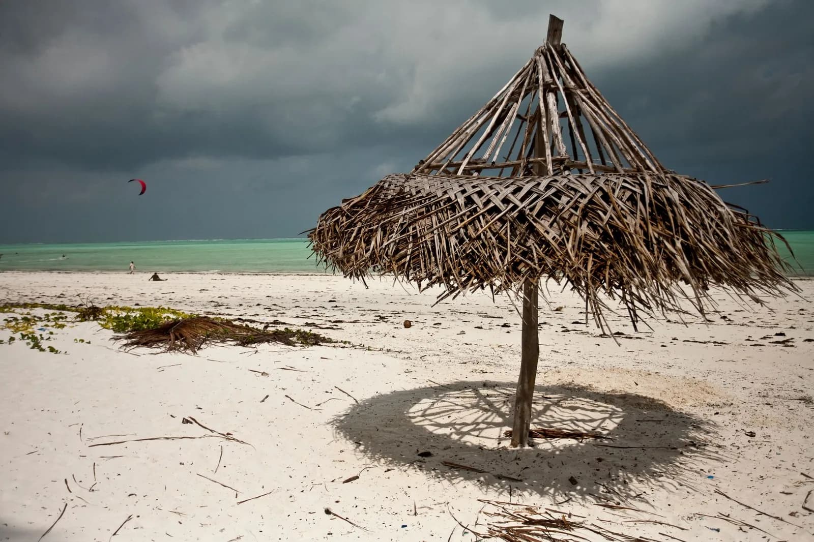 Parasol de palme sur le sable blanc d'une plage de Zanzibar face au lagon turquoise, sous un ciel d'averse tropicale en décembre