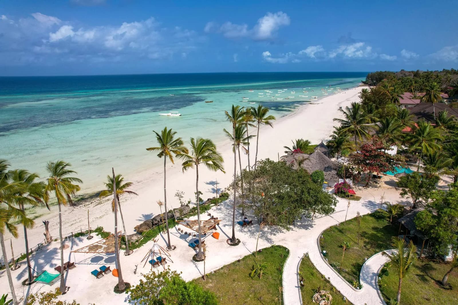 Vue aérienne d'une plage de sable blanc bordée de palmiers et d'un resort à Zanzibar, lagon turquoise et bateaux de pêche au large