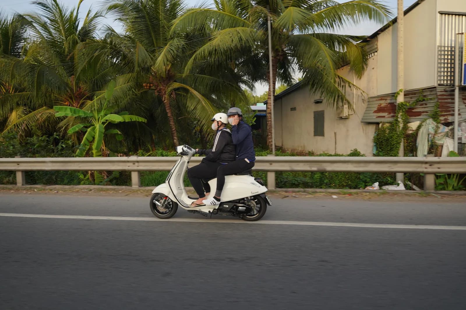 Deux voyageurs à scooter sur une route bordée de palmiers, un moyen de transport courant à Zanzibar