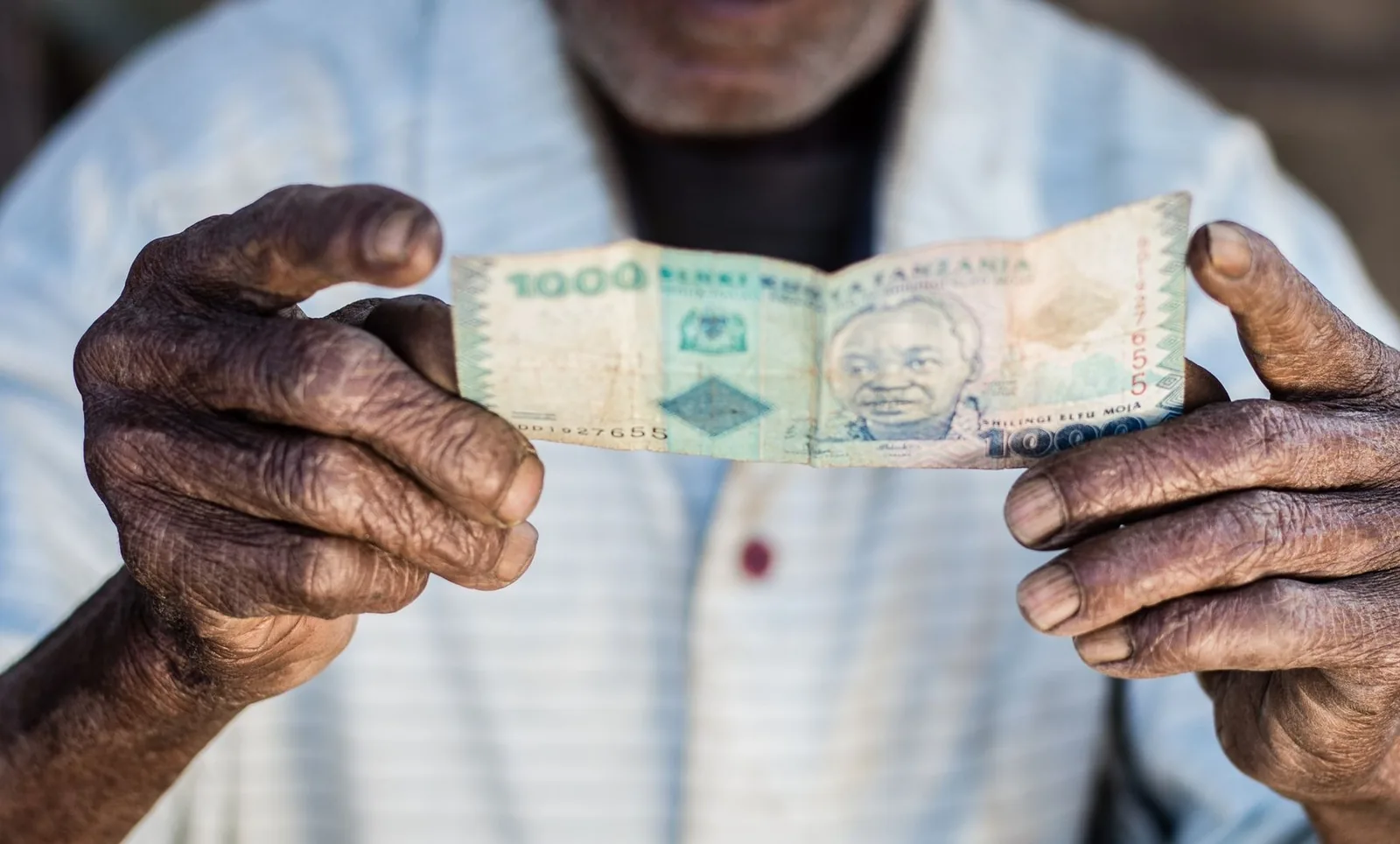 Mains tenant un billet de 1 000 shillings tanzaniens de la Bank of Tanzania, à l'effigie de Julius Nyerere