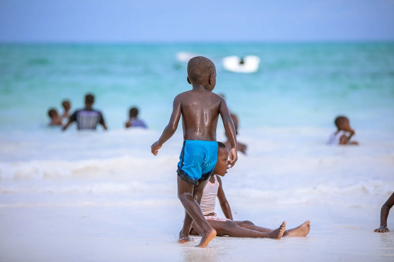 Enfants jouant au bord du lagon turquoise sur une plage de sable blanc à Zanzibar